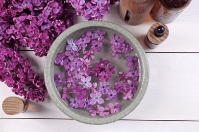 Cosmetic products and lilac flowers on white wooden table, flat lay