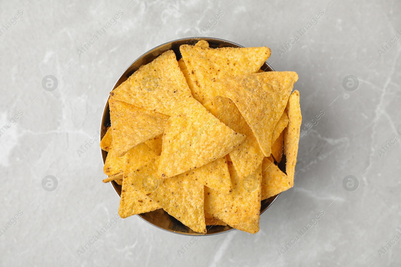 Photo of Metal bowl with tasty Mexican nachos chips on grey table, top view