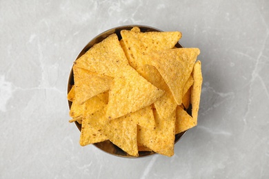 Metal bowl with tasty Mexican nachos chips on grey table, top view