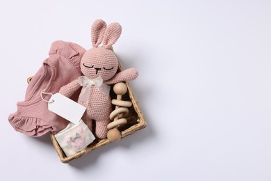 Photo of Different baby accessories, clothes and blank card in wicker box on white background, top view. Space for text