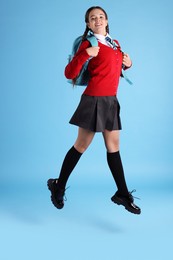 Teenage girl in school uniform with backpack jumping on light blue background