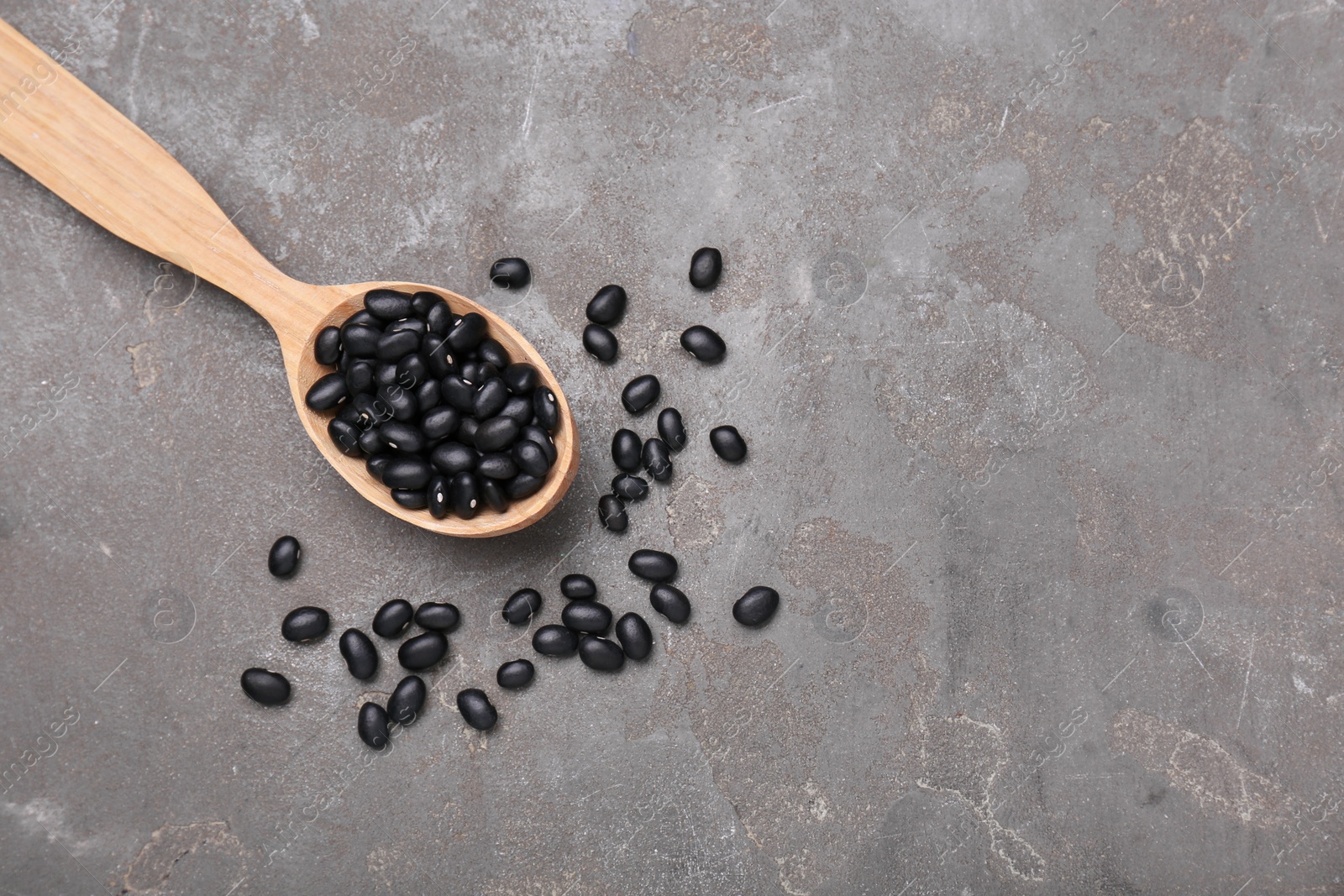 Photo of Spoon of raw black beans on grey table, top view. Space for text