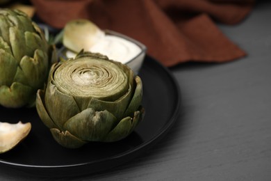 Photo of Delicious cooked artichokes with tasty sauce on grey wooden table, closeup. Space for text