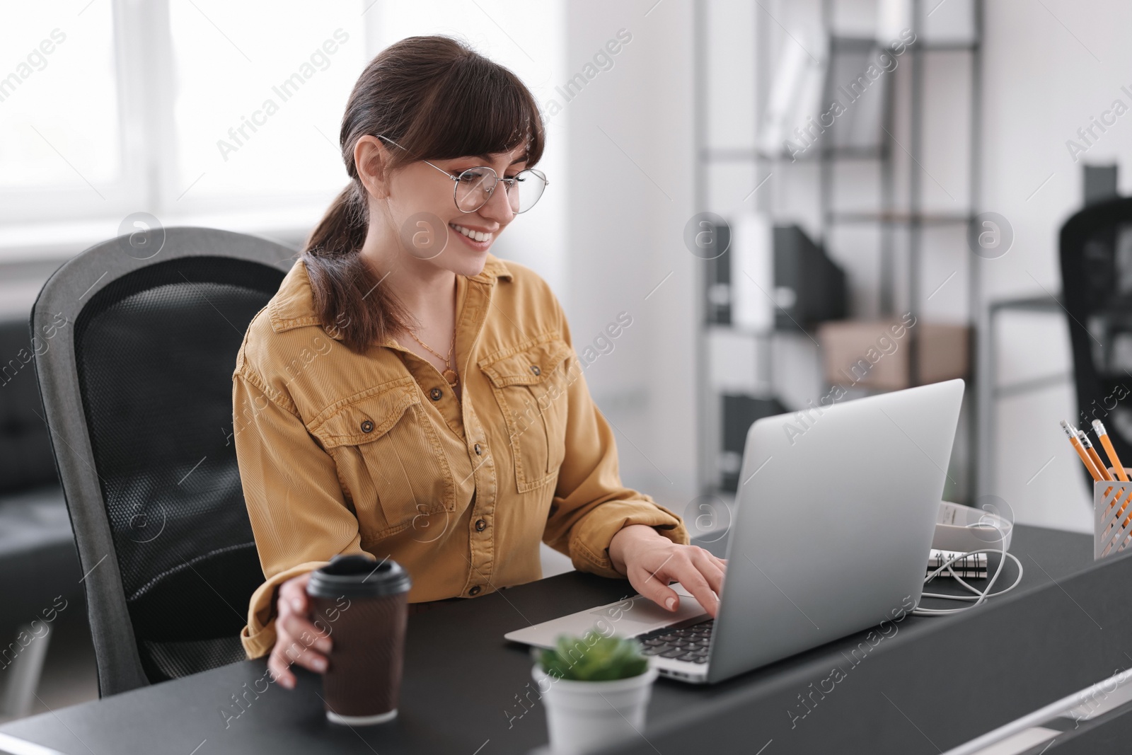 Photo of Woman with cup of coffee watching webinar at table in office