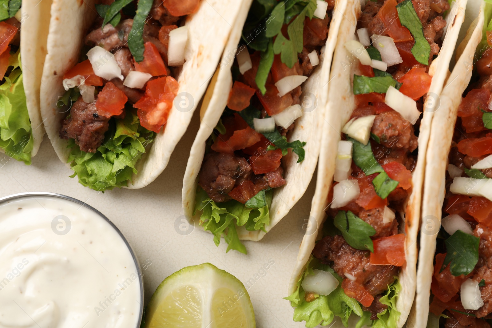 Photo of Delicious meat tacos with vegetables, lime and sauce on light table, flat lay