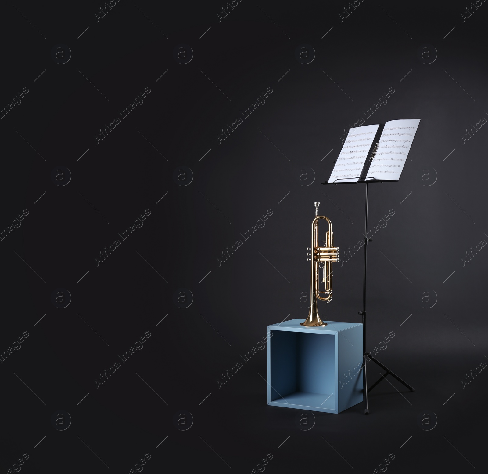 Photo of Trumpet and note stand with music sheets on black background. Space for text