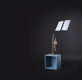 Photo of Trumpet and note stand with music sheets on black background. Space for text