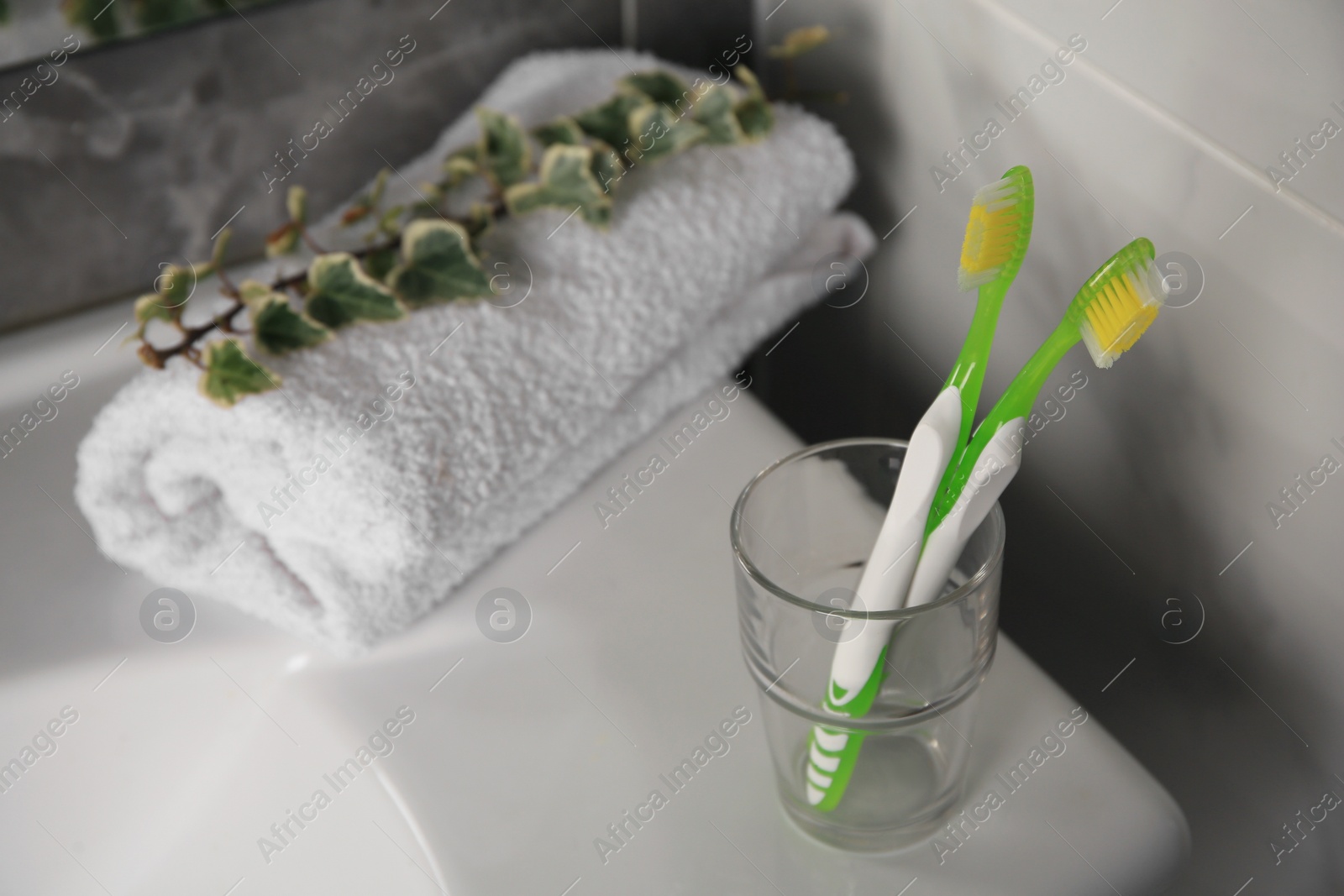 Photo of Light green toothbrushes in glass holder on washbasin