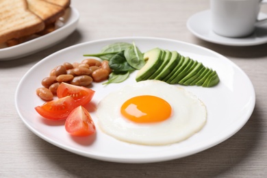 Photo of Tasty breakfast with fried egg, beans and avocado served on white wooden table, closeup