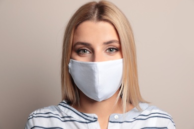 Young woman in protective face mask on beige background