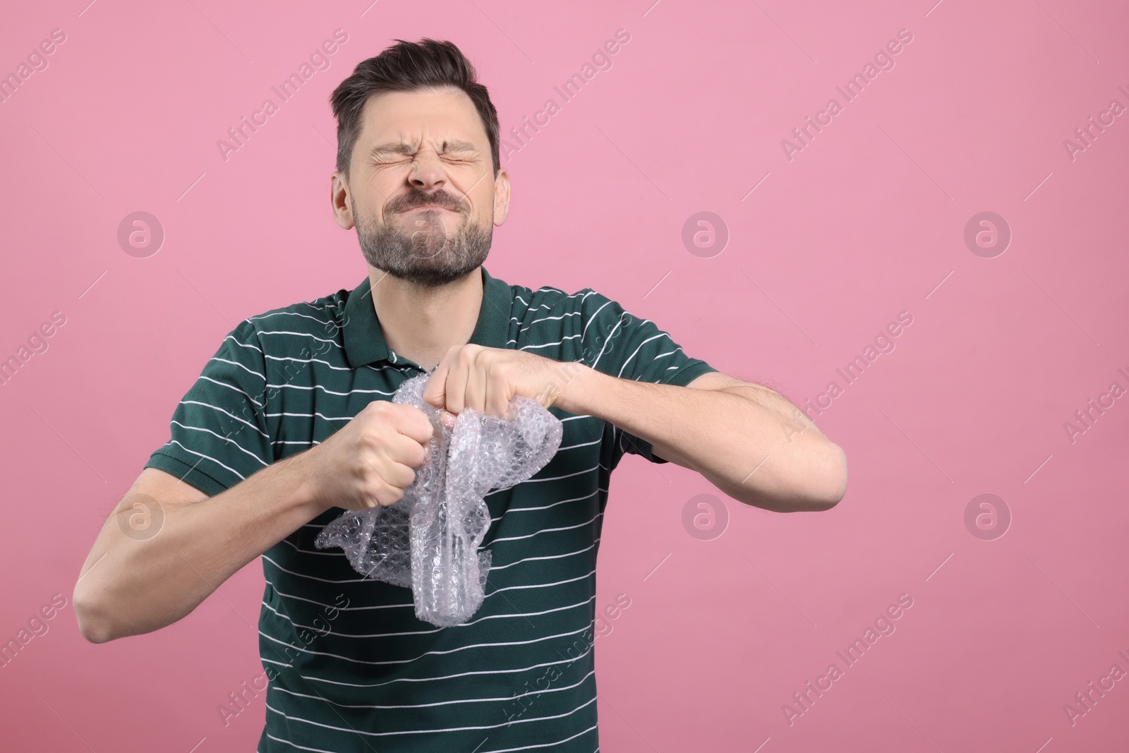 Photo of Man popping bubble wrap on pink background, space for text. Stress relief