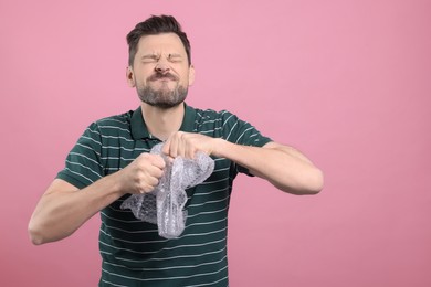 Man popping bubble wrap on pink background, space for text. Stress relief