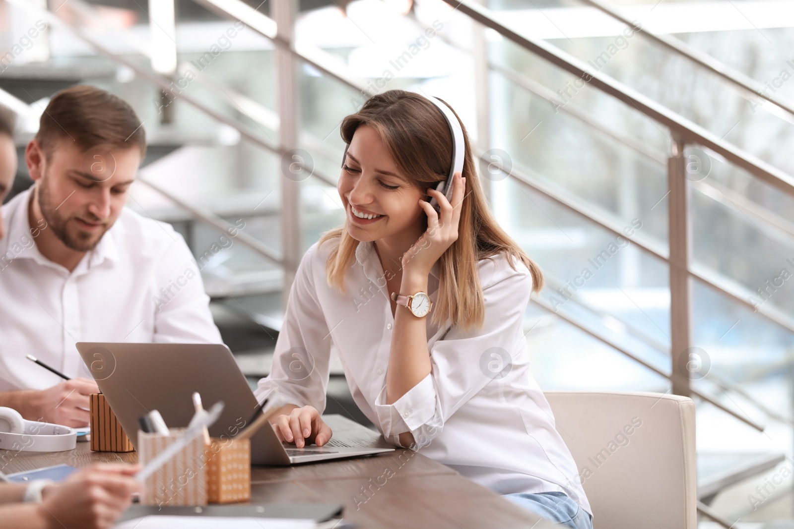 Photo of Young businesswoman with headphones, laptop and her colleagues working in office