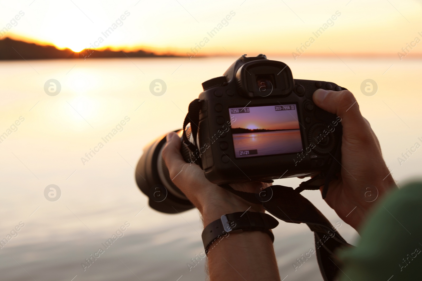 Photo of Male photographer holding professional camera with photo of riverside sunset on display