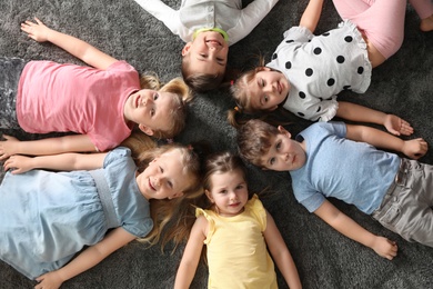 Photo of Playful little children lying on carpet indoors, top view