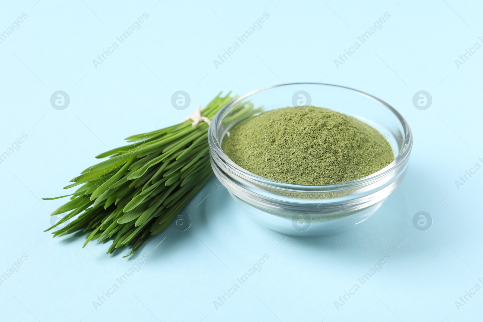 Photo of Wheat grass powder in glass bowl and fresh sprouts on light blue table