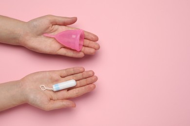 Photo of Woman holding menstrual cup and tampon on pink background, top view. Space for text