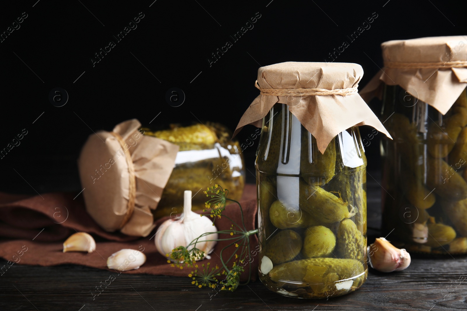 Photo of Jars with pickled cucumbers on wooden table against black background