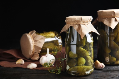 Jars with pickled cucumbers on wooden table against black background