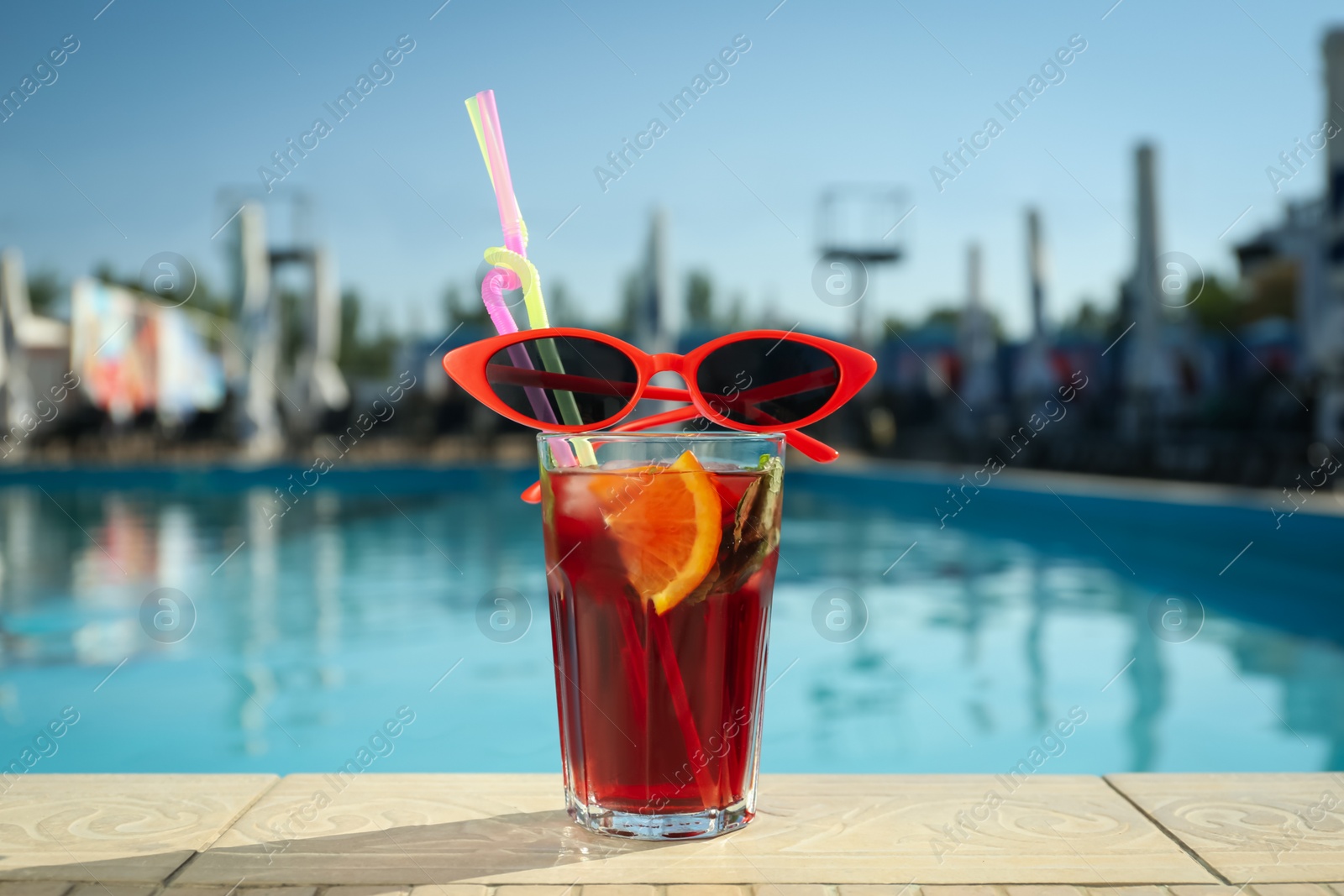 Photo of Tasty refreshing cocktail and sunglasses on edge of swimming pool. Party items