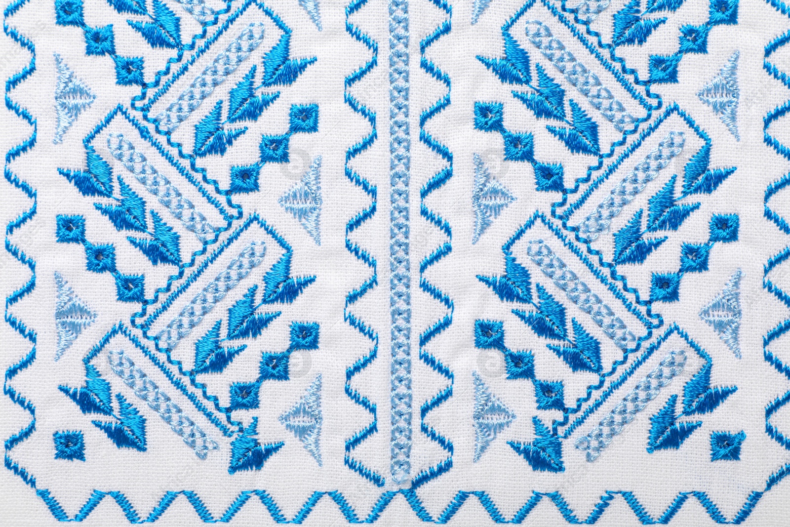 Photo of Beautiful light blue Ukrainian national embroidery on white fabric, top view