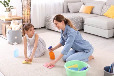 Housewife with daughter cleaning carpet in room together