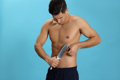 Fit man with knife and marks on body against light blue background. Weight loss surgery