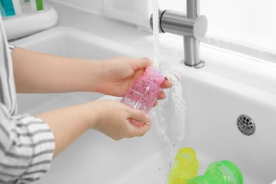 Photo of Woman washing baby bottle under stream of water in kitchen, closeup