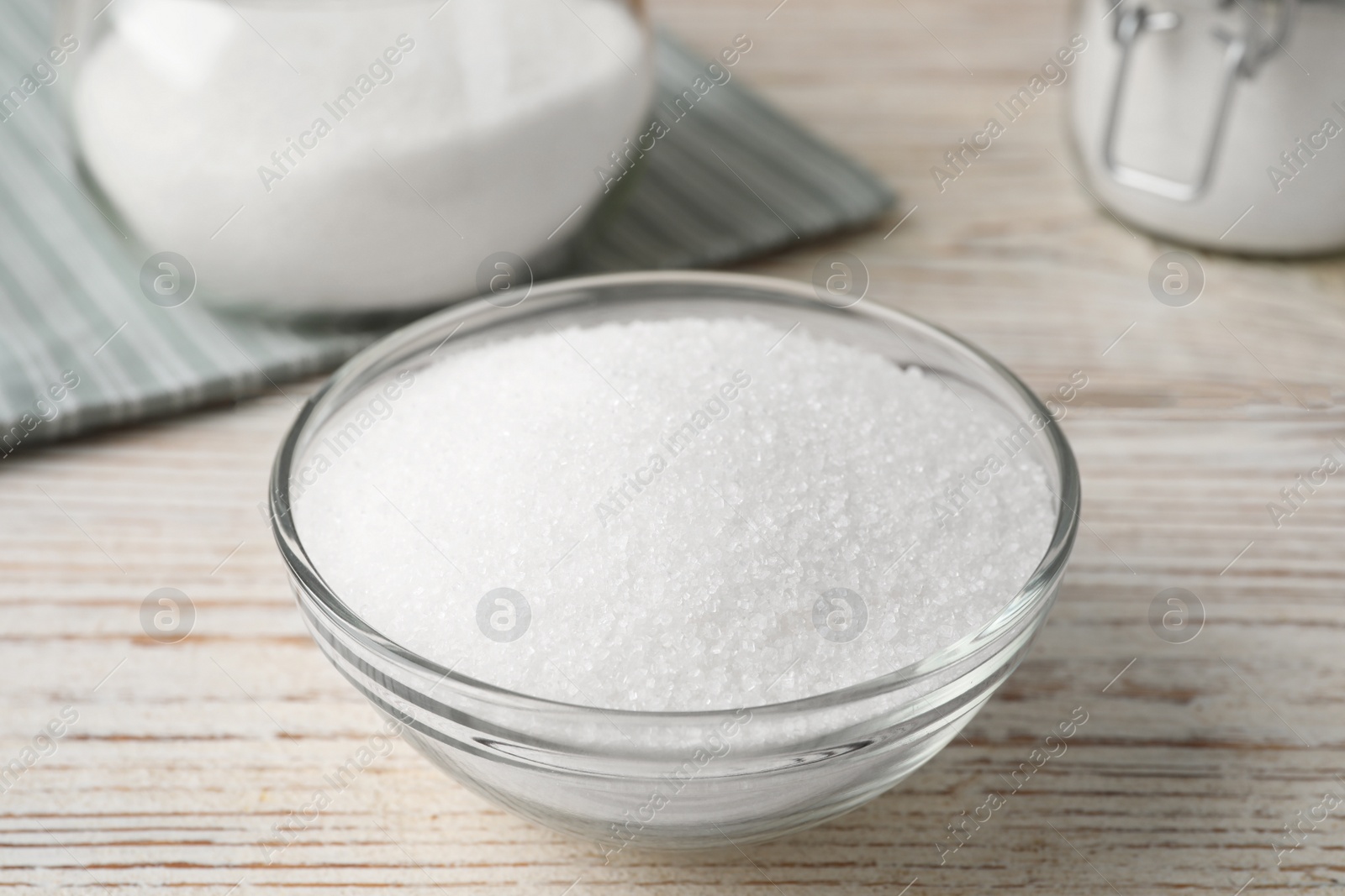 Photo of Granulated sugar in glass bowl on white wooden table, closeup