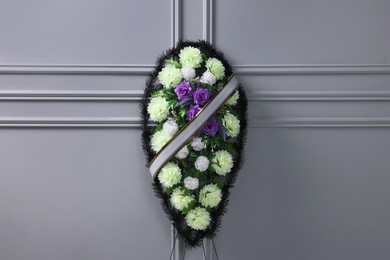 Funeral wreath of plastic flowers with ribbon near light grey wall