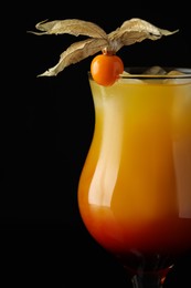 Photo of Tasty cocktail decorated with physalis fruit on black background, closeup