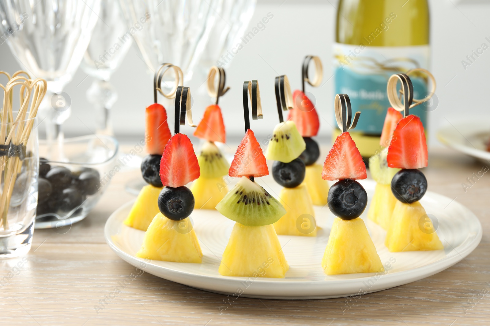 Photo of Tasty canapes with pineapple, kiwi and berries on light wooden table, closeup