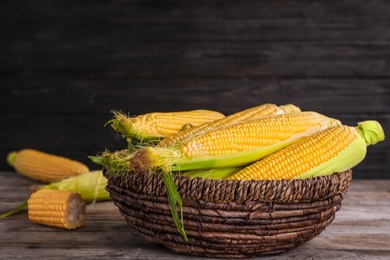 Photo of Basket with tasty sweet corn cobs on table