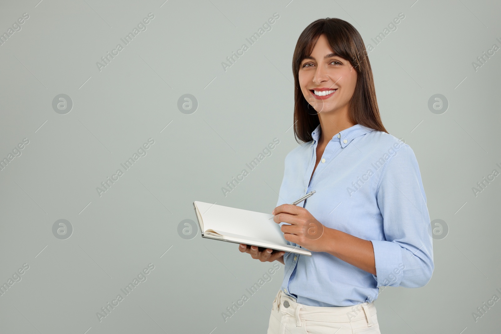 Photo of Happy secretary with notebook and pen on light grey background. Space for text