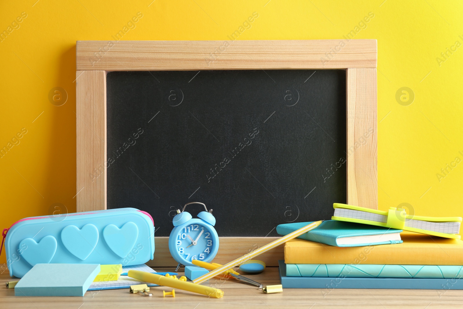 Photo of Different school stationery and small blank chalkboard on table near yellow wall. Space for text