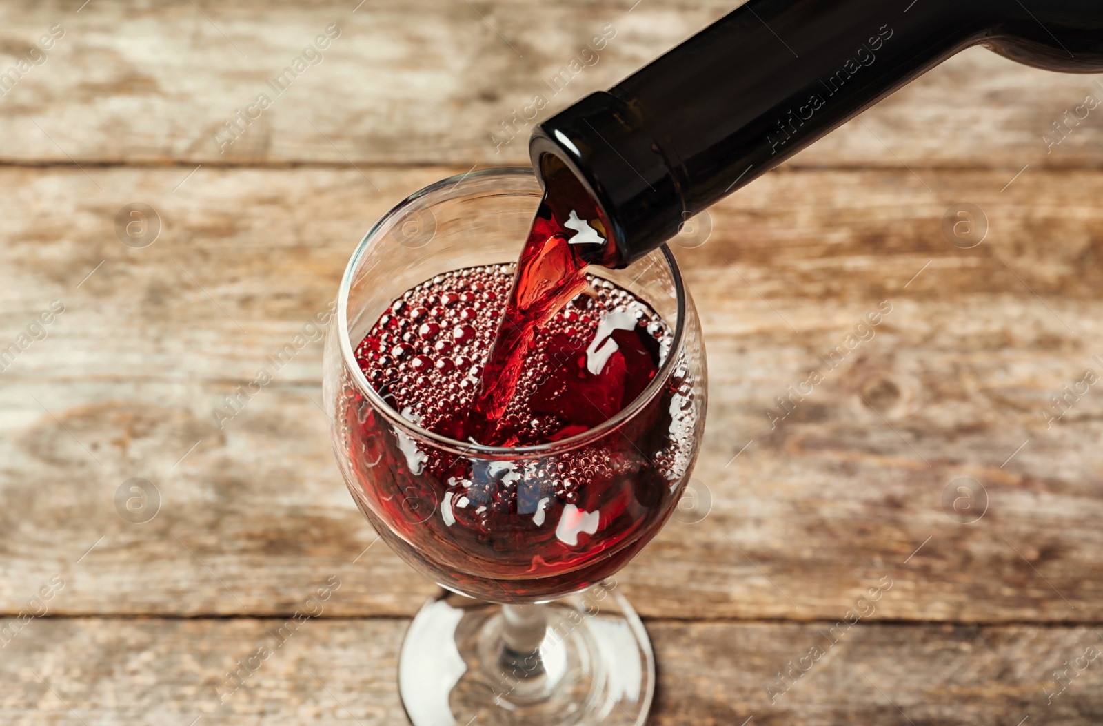 Photo of Pouring delicious red wine into glass on wooden background