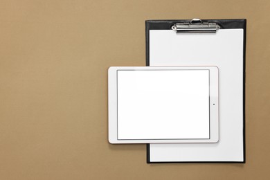 Modern tablet and clipboard on dark beige background, flat lay. Space for text