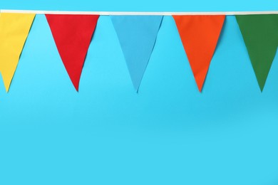 Bunting with colorful triangular flags on light blue background. Space for text