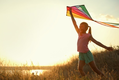 Photo of Cute little child with kite running outdoors at sunset. Spending time in nature