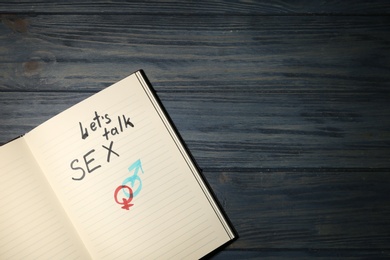 Photo of Notebook with phrase "LET'S TALK SEX" and gender symbols on dark wooden background, top view. Space for text