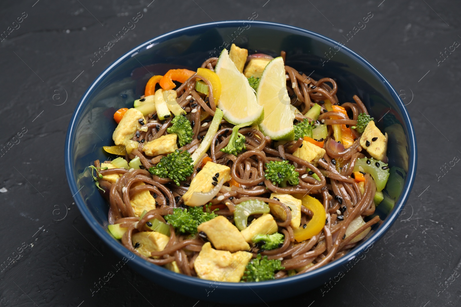 Photo of Stir-fry. Delicious cooked noodles with chicken and vegetables in bowl on gray textured table, closeup