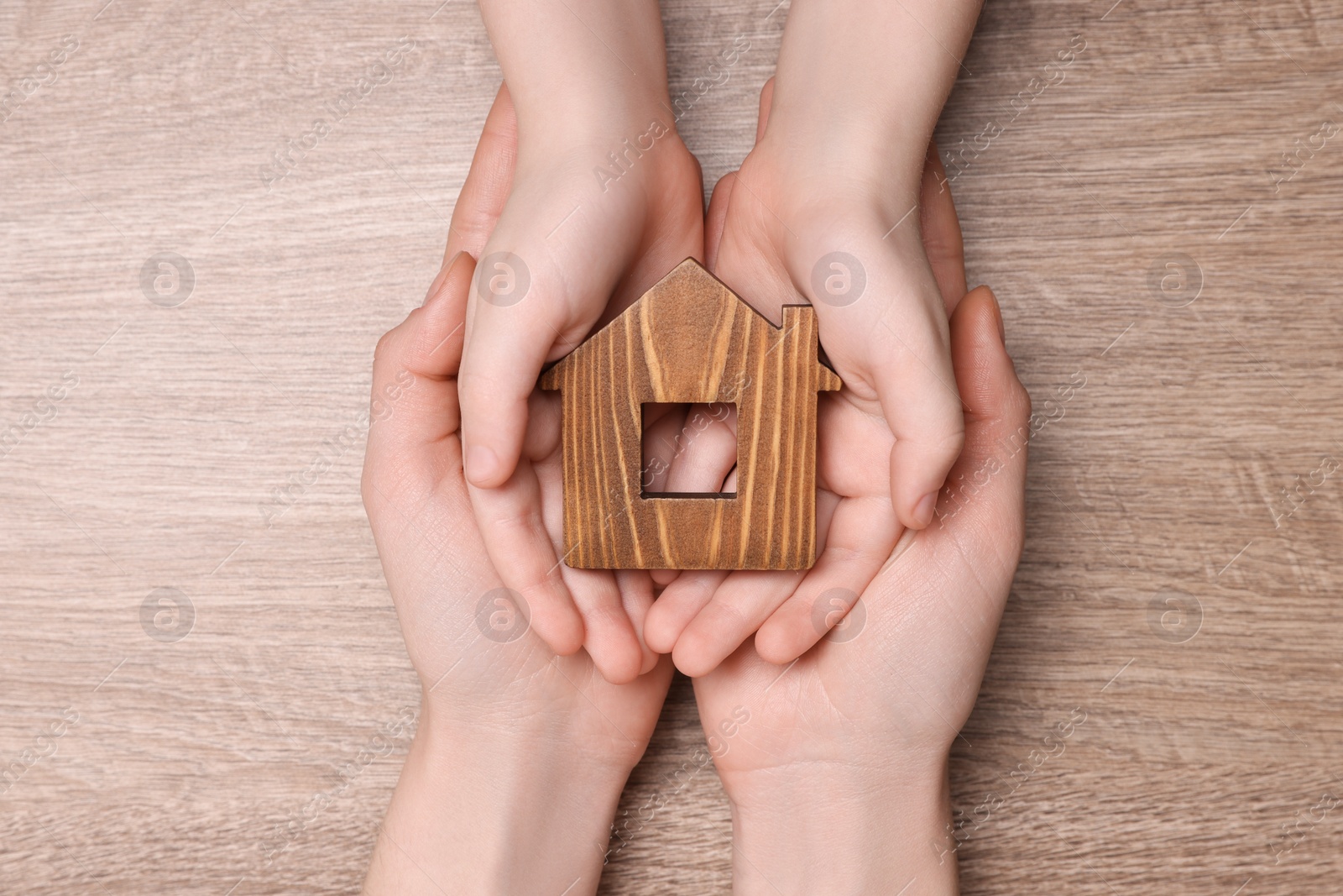 Photo of Home security concept. Woman with her little child holding house model at wooden table, top view
