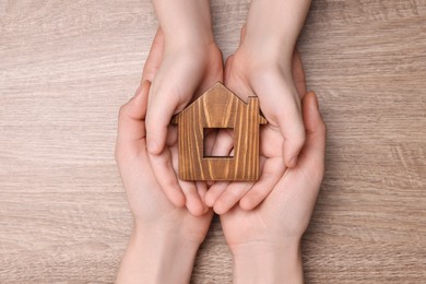 Home security concept. Woman with her little child holding house model at wooden table, top view