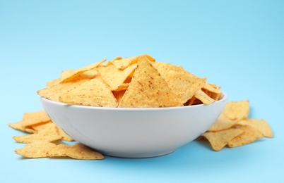 Bowl of tasty Mexican nachos chips on light blue background