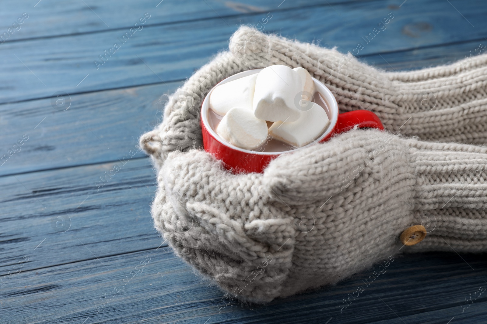 Photo of Person holding cup of tasty cocoa with marshmallows on blue wooden table, closeup