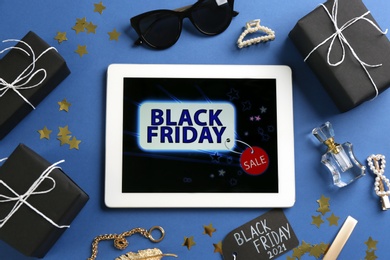 Photo of Flat lay composition with tablet, gifts and accessories on blue background. Black Friday sale