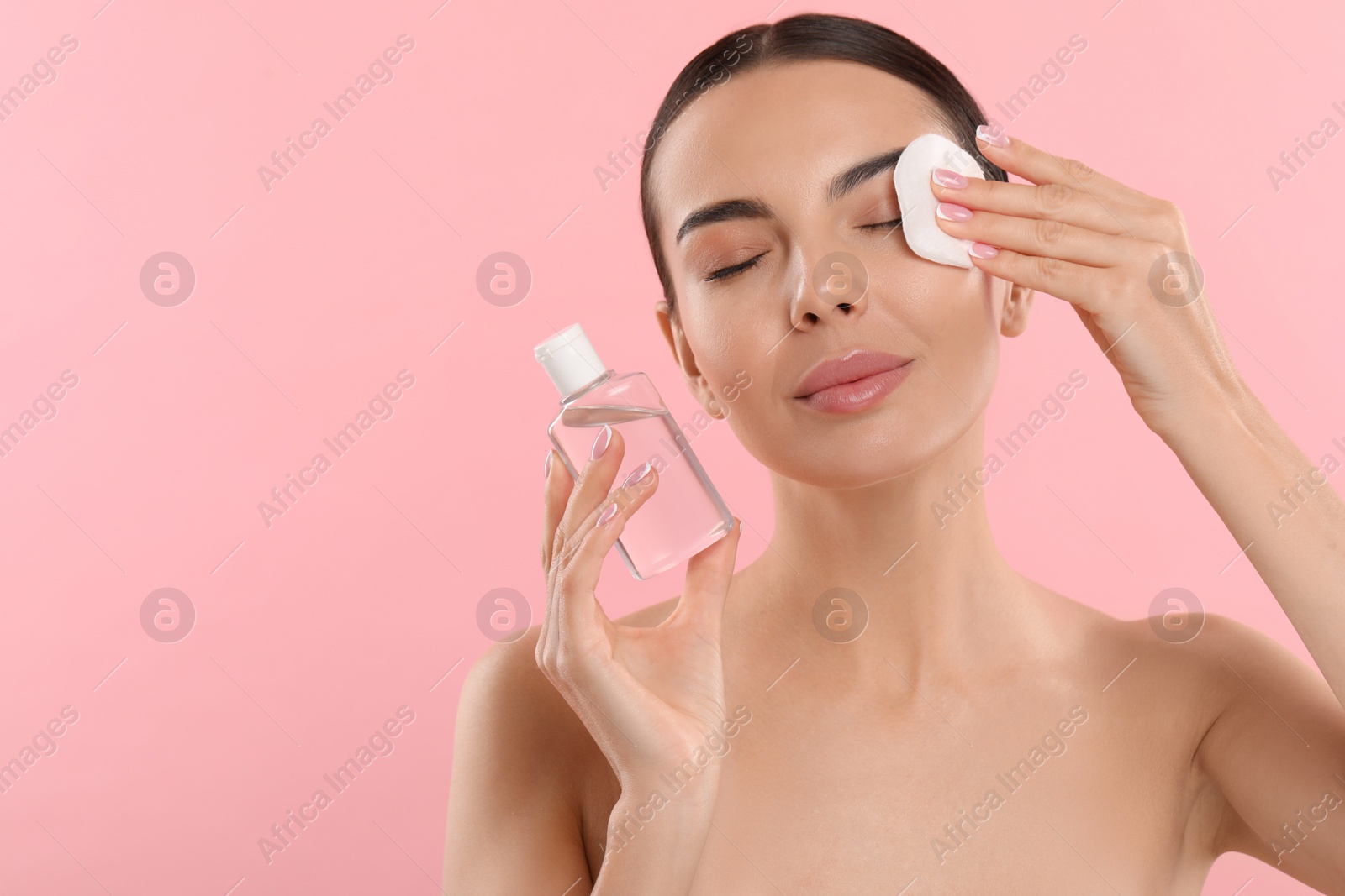 Photo of Beautiful woman removing makeup with cotton pad on pink background, space for text