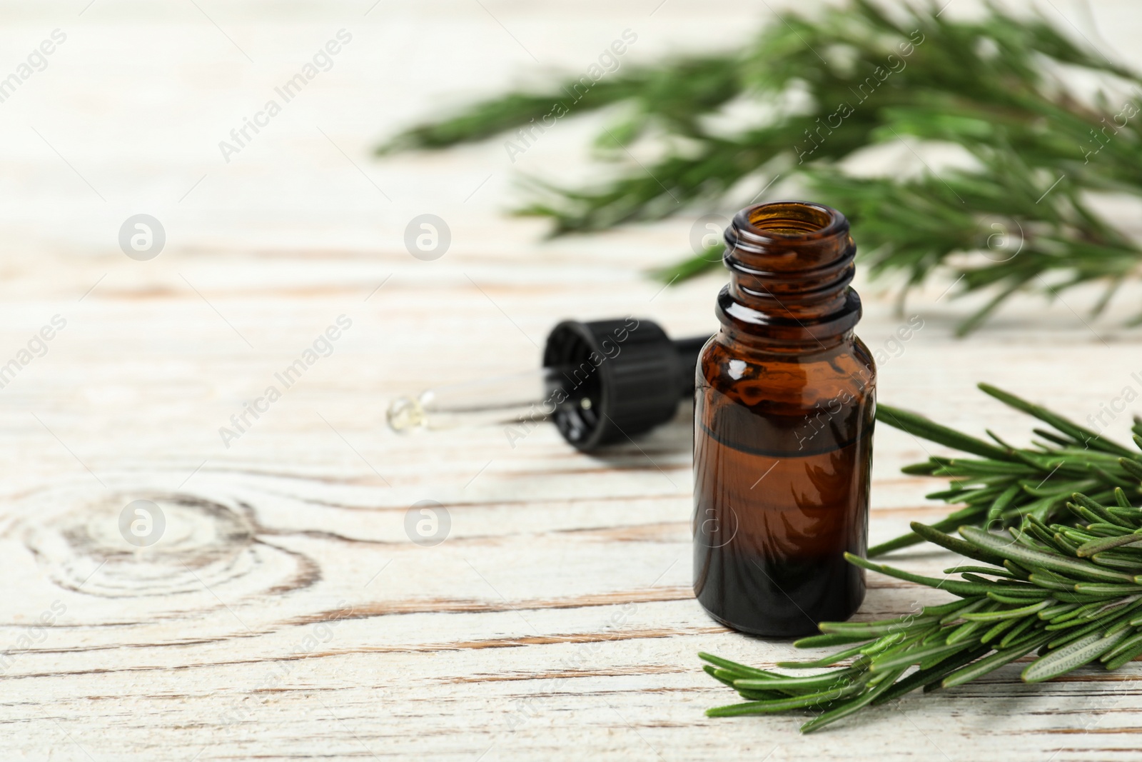 Photo of Bottle of rosemary essential oil on white wooden table. Space for text