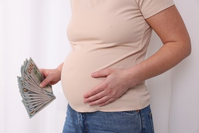 Photo of Surrogate mother. Pregnant woman with dollar banknotes indoors, closeup