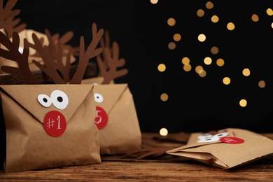 Gifts in envelopes with deer faces on wooden table against blurred lights, space for text. Christmas advent calendar